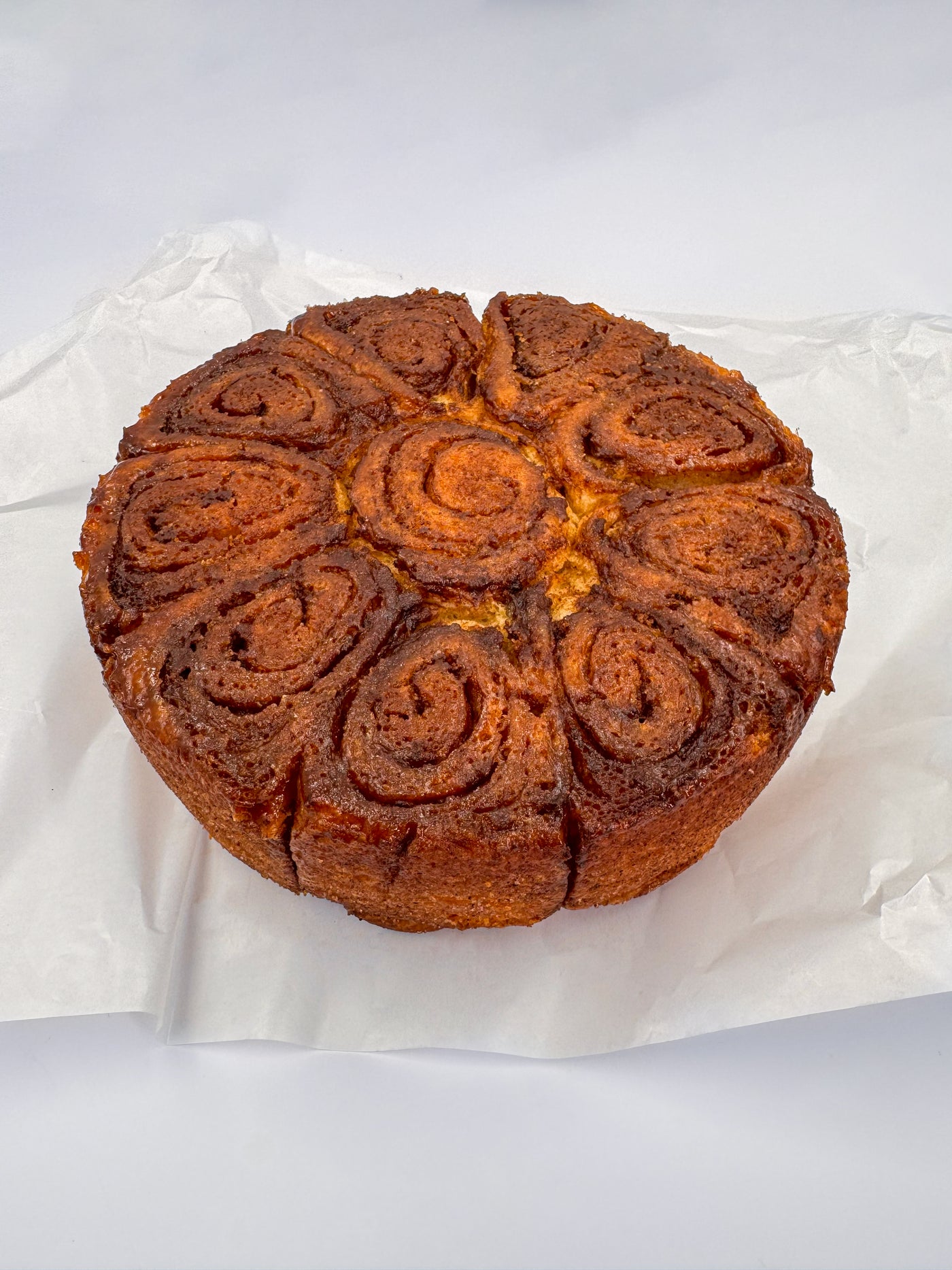 A Cinnamon Scroll from Loafology Bakery & Café, with a caramelized swirl top, rests on white parchment paper against a plain background.