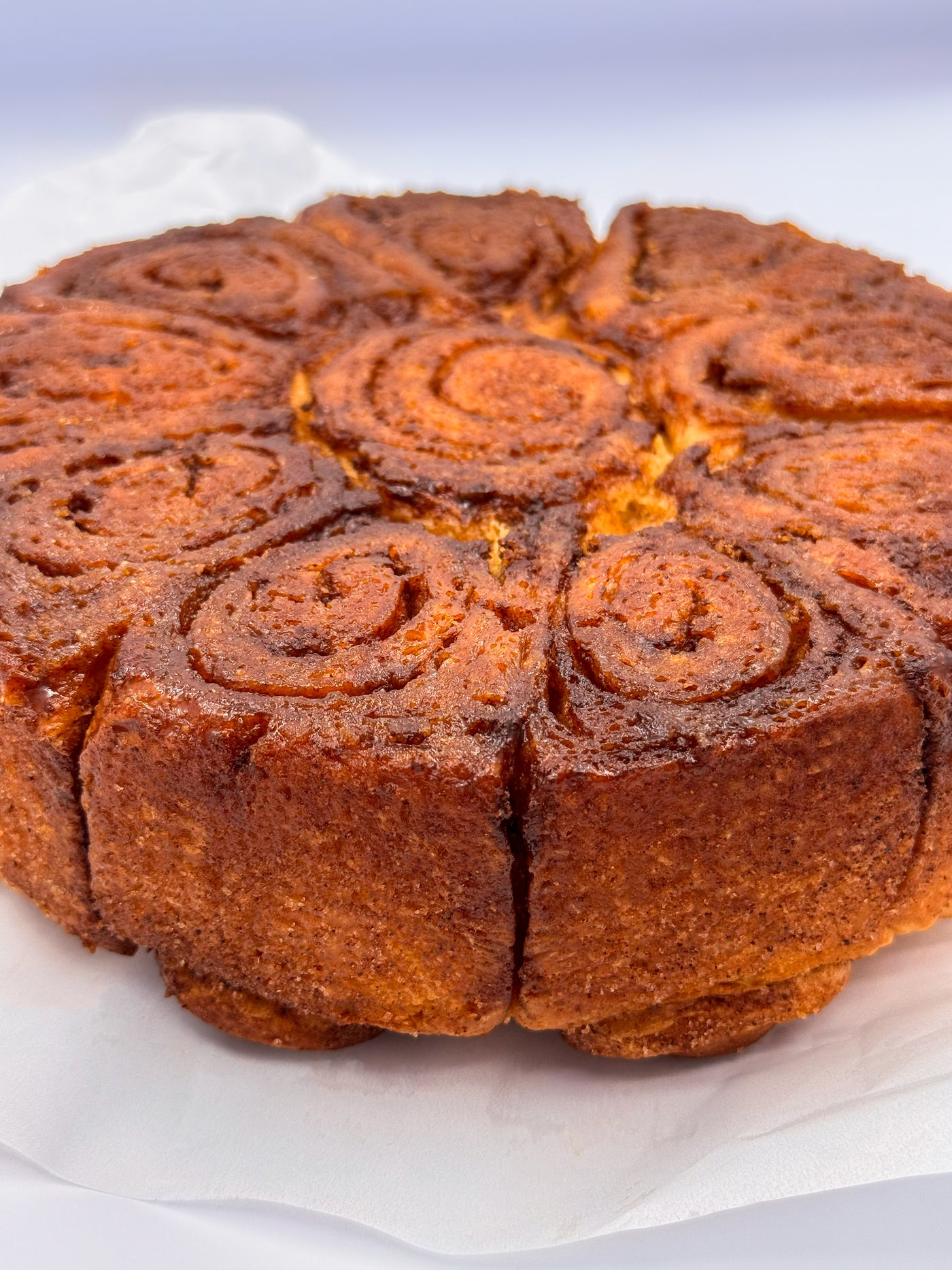 A close-up of Cinnamon Scrolls by Loafology Bakery & Café, baked golden brown and sliced into spiral pieces, resting on white parchment paper.