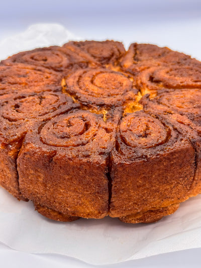 A close-up of Cinnamon Scrolls by Loafology Bakery & Café, baked golden brown and sliced into spiral pieces, resting on white parchment paper.