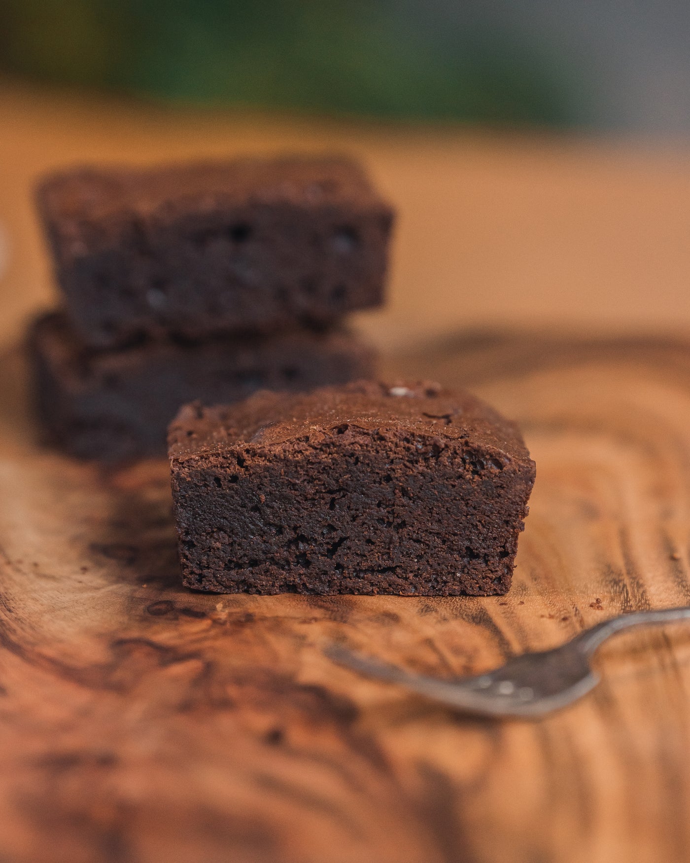 A close-up of a stack of three Chocolate Truffle Brownies from Loafology Bakery & Café on a wooden surface, with a fork placed nearby.