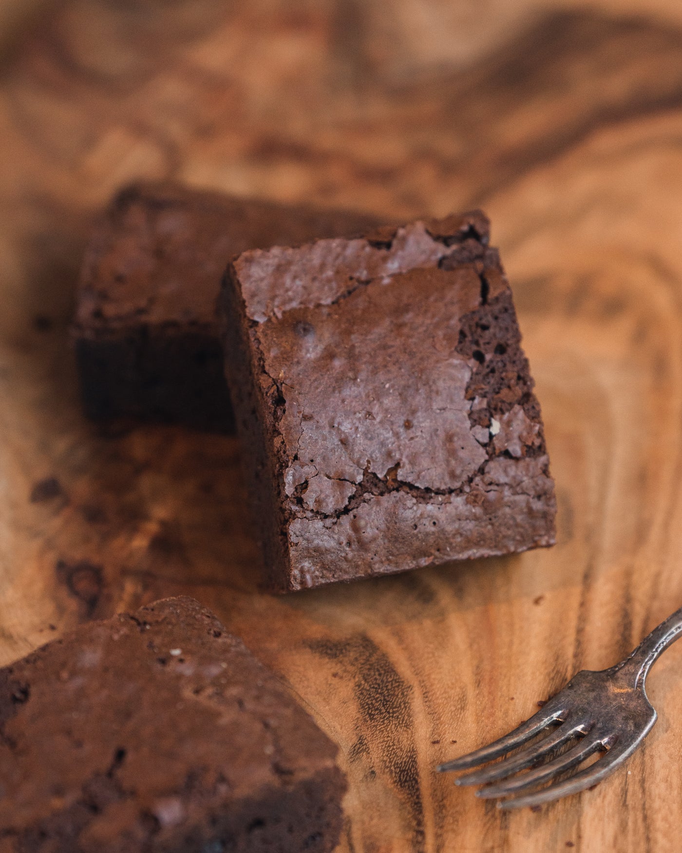 Close-up of two square pieces of Chocolate Truffle Brownie by Loafology Bakery & Café on a wooden surface with a fork to the side.