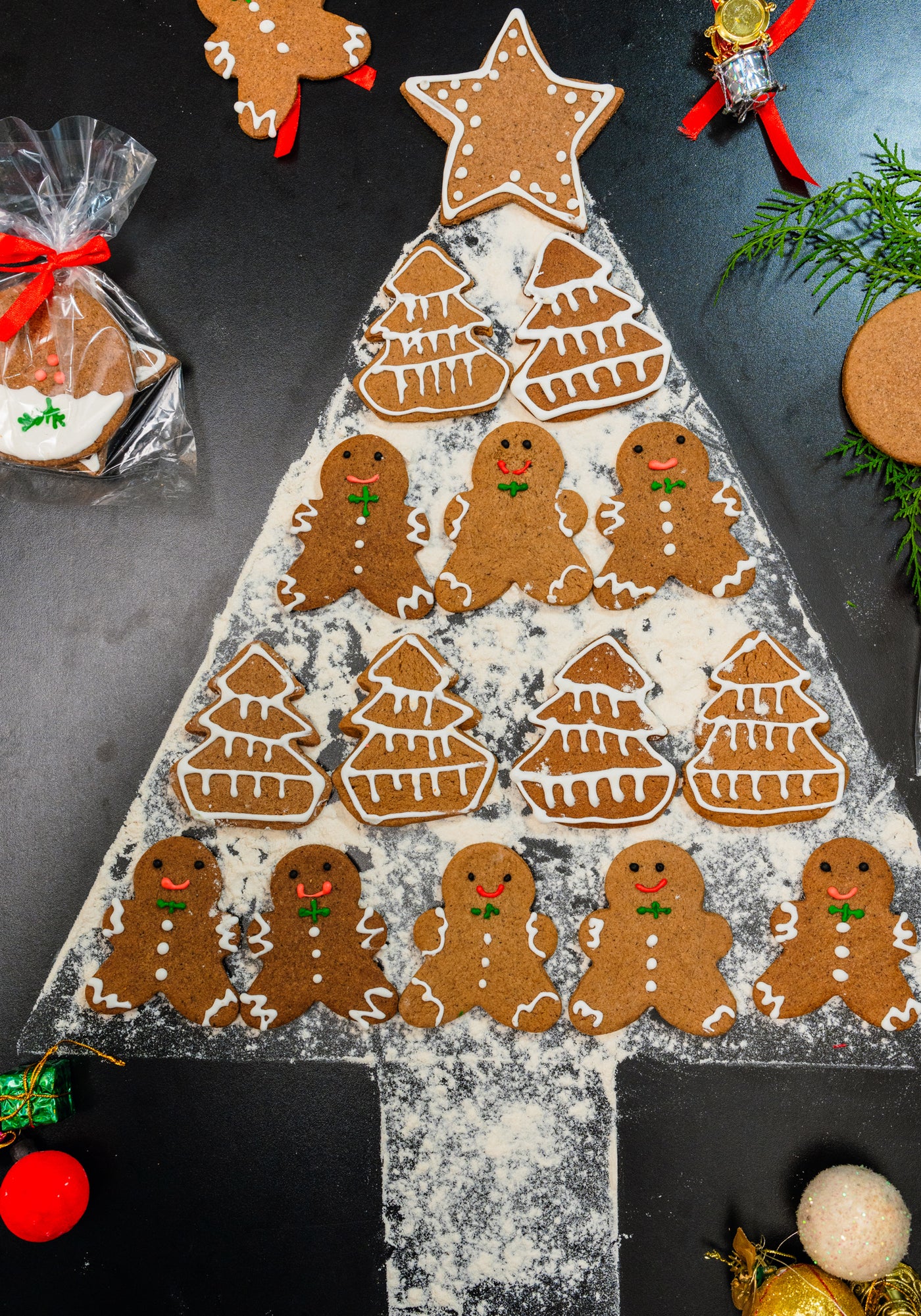 Christmas Ginger Cookies from Loafology Bakery & Café are artfully arranged as gingerbread men and trees in a festive display on a flour-dusted black surface, capturing the holiday spirit and delighting the senses.