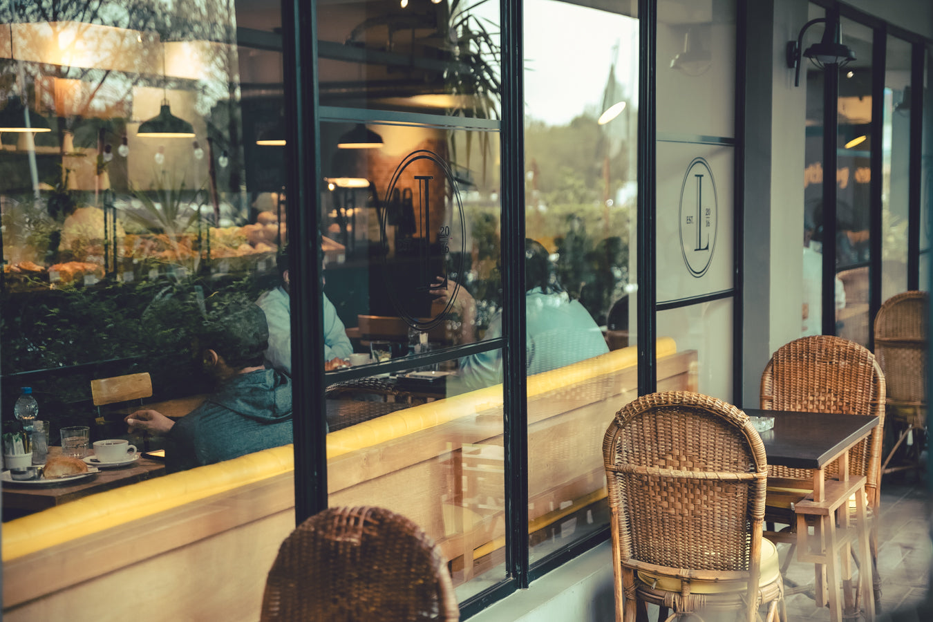 Exterior view of Loafology Bakery & Café with indoor patrons visible through large windows and empty rattan chairs and tables set on the patio area.