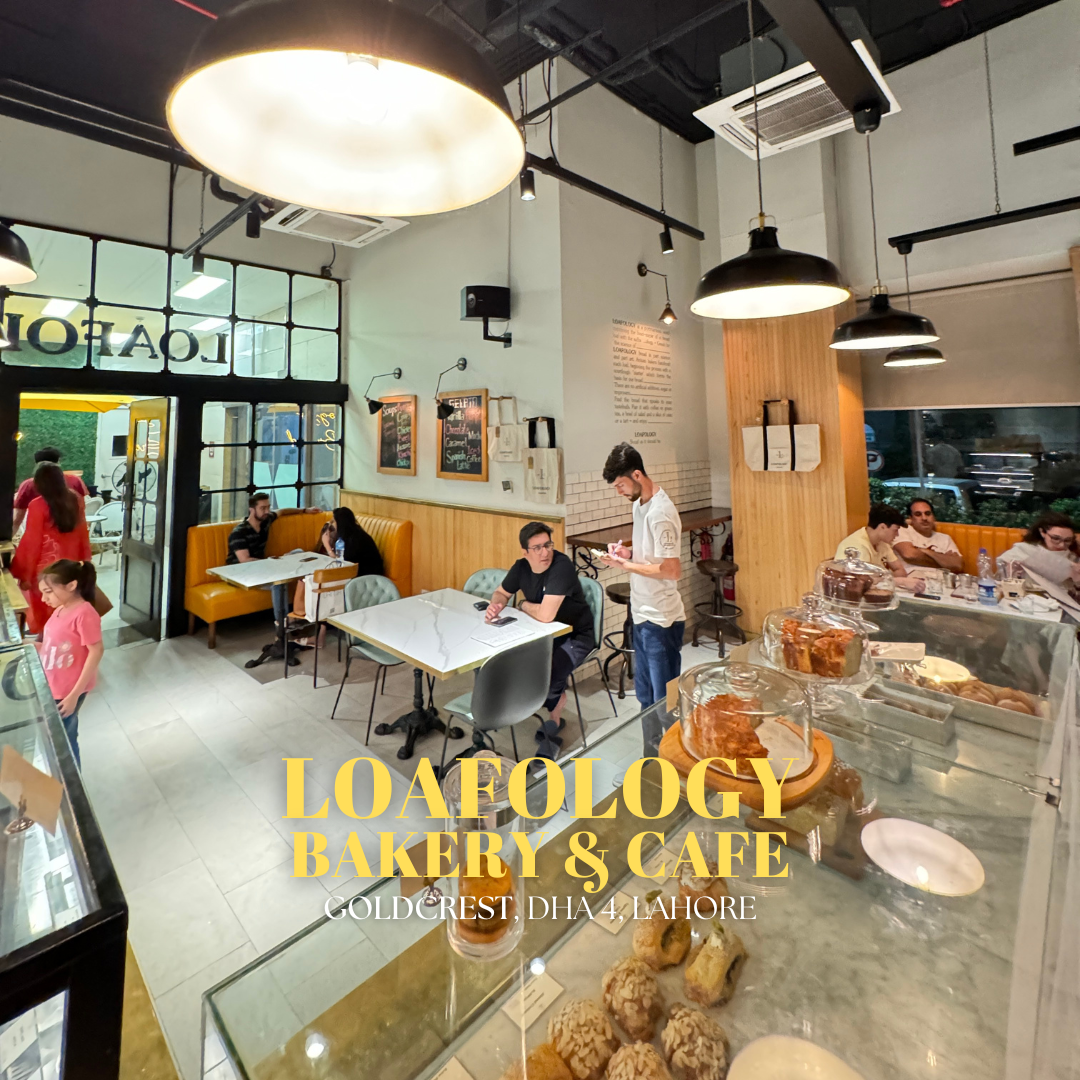 The interior of Loafology Bakery & Café Goldcrest DHA4 Lahore, features customers enjoying food at tables. Glass display cases are filled with a variety of pastries and baked goods. Warm lighting and a cozy ambiance complete the inviting atmosphere.