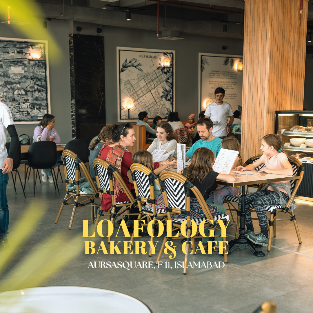 A group of people are sitting around tables with chairs inside Loafology Bakery & Café in Aursasquare, F-11, Islamabad. The bakery's name and location can be seen at the bottom of the image.