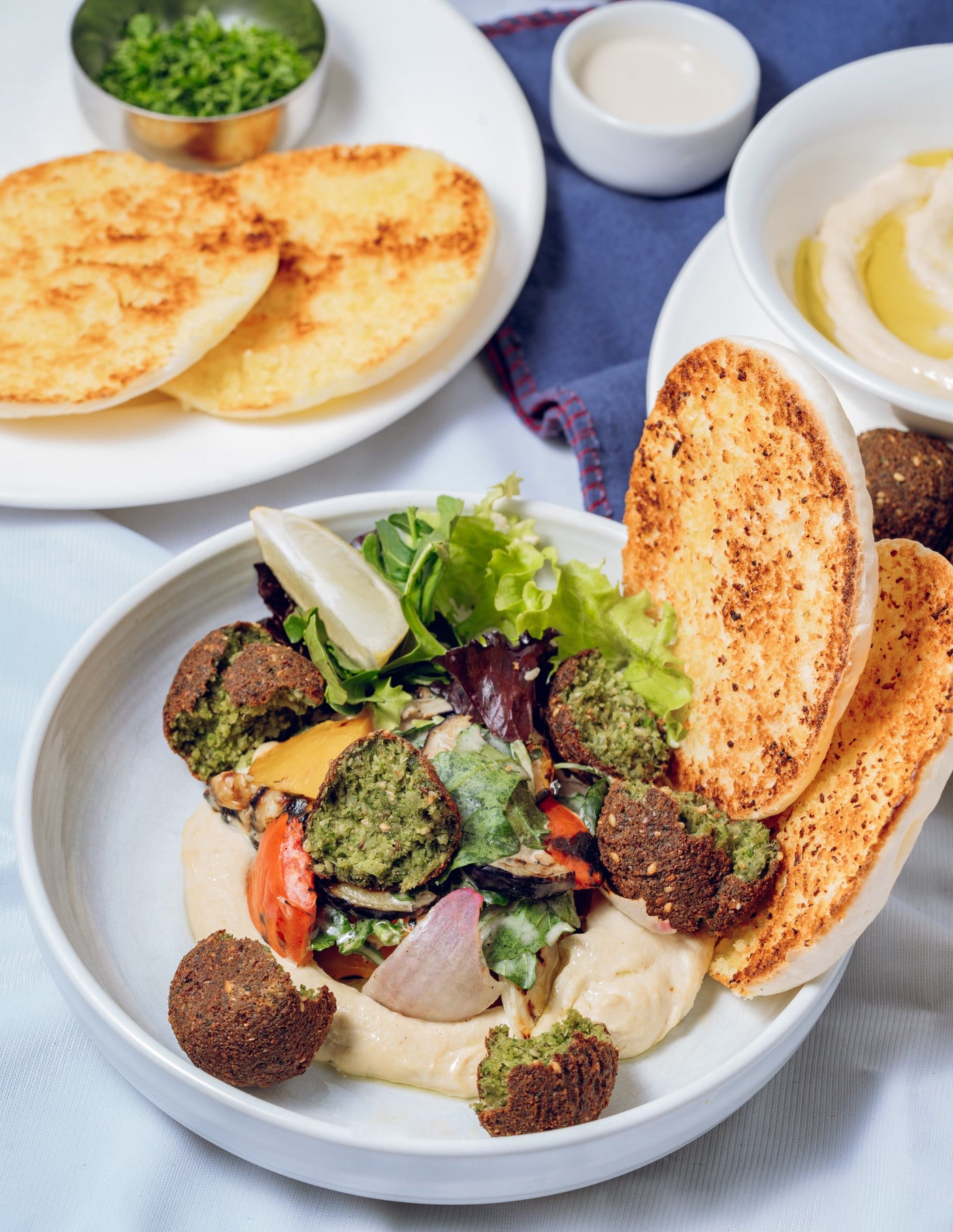 Enjoy Loafology Bakery & Café's Hummus and Falafel Bowl with falafel, creamy hummus, mixed greens, vibrant veggies, and warm pita. On the side, extra pita and fresh herbs accompany a classic hummus bowl for an authentic Middle Eastern dining experience.
