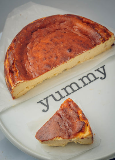 A partially sliced San Sebastián Cheese Cake from Loafology Bakery & Café rests on a plate with "yummy" written next to it, tempting you to indulge in its rich, creamy goodness.