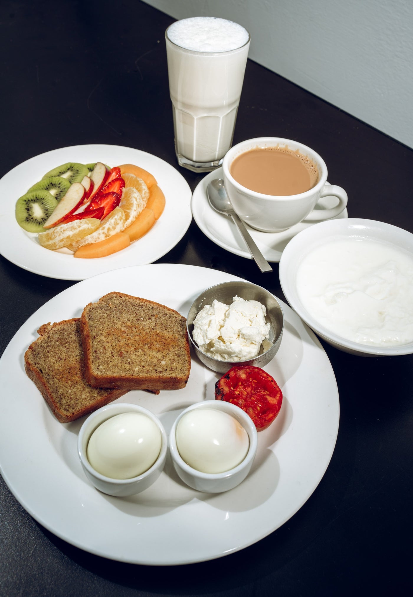 A breakfast spread includes Loafology Bakery & Café's Keto Sehri, boiled eggs, cream cheese toast, sliced tomato, plain yogurt, mixed fruit plate, a glass of milk, and coffee.