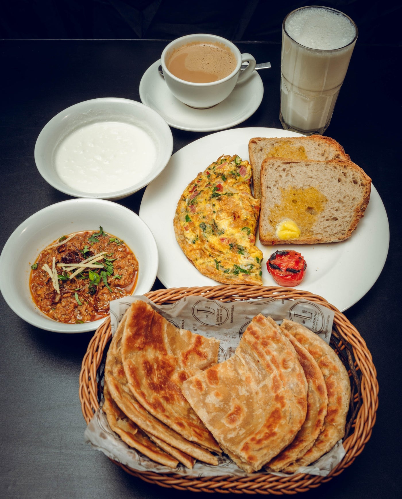 The Desi Sehri 2 from Loafology Bakery & Café promises a breakfast spread featuring parathas in a basket, a Desi omelette with buttered toast, curry, yogurt, chai, and refreshing lassi.