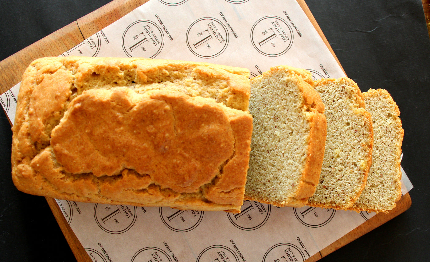 Keto Bread from Loafology Bakery & Café, with a golden crust, rests on parchment paper while three slices are displayed on a wooden cutting board.