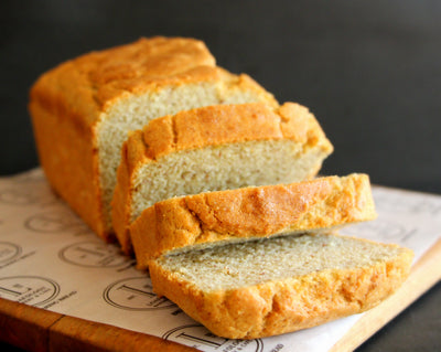 Three slices cut from a loaf of Keto Bread by Loafology Bakery & Café rest on patterned paper placed on a wooden board.