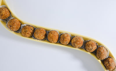 A curved, yellow tray from Loafology Bakery & Café holds ten uniformly-sized, round Energy Bites, each placed in a white paper cup and lined in a single row.