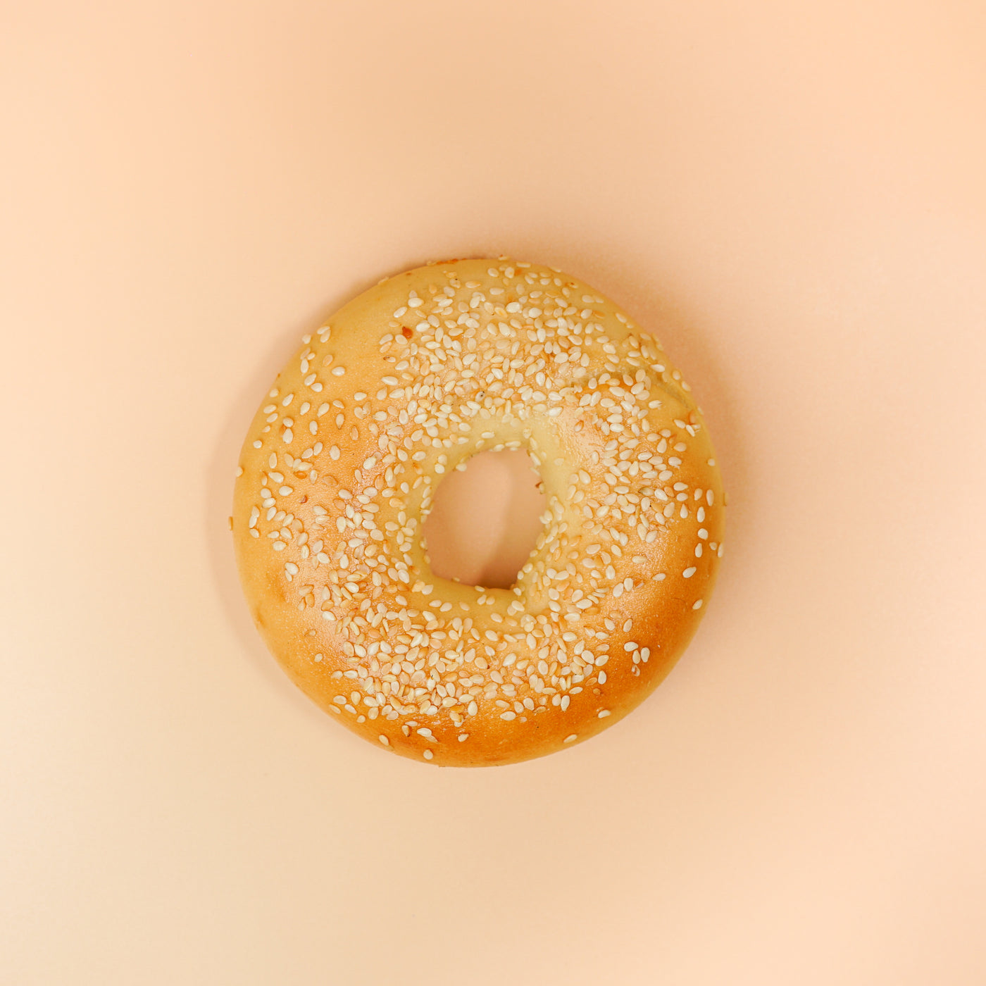 At the heart of a light peach-colored background sits the "Breakfast Fix" from Loafology Bakery & Café—a plain bagel adorned with sesame seeds, subtly suggesting the perfect pairing of creamy cream cheese.