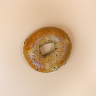 A "Breakfast Fix" plain bagel from Loafology Bakery & Café, viewed from above and paired with a smooth spread of cream cheese, placed against a beige background.