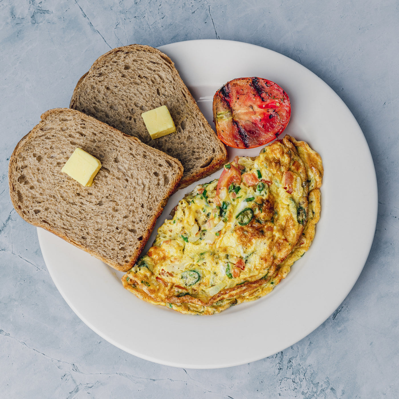 A Desi Omelette made from organic eggs, served with two slices of house sourdough toast with butter and a roasted tomato, all by Loafology Bakery & Café.