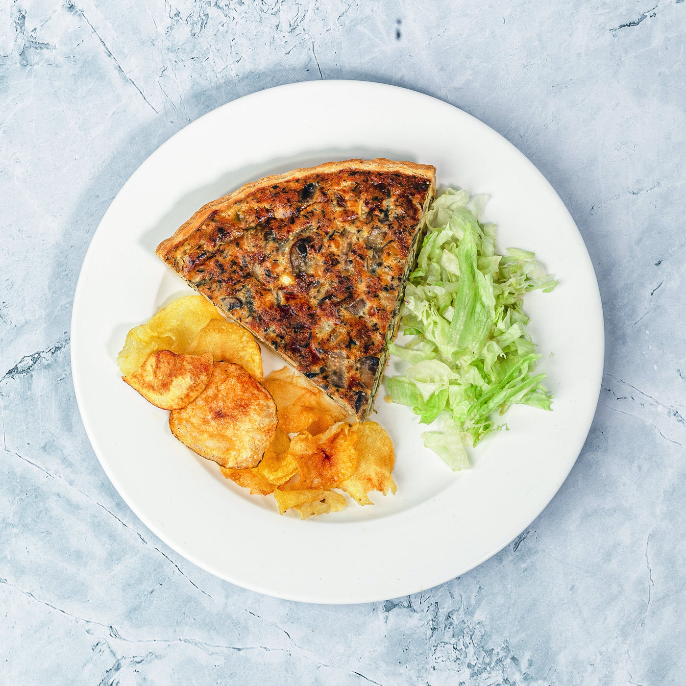 A plate with a slice of Loafology Bakery & Café's Mushroom Quiche, accompanied by a portion of potato chips and a side of shredded lettuce on a marble surface.