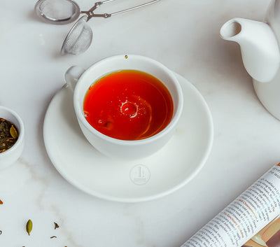 A cup of aromatic Spicy Chai from Loafology Bakery & Café on a white saucer, accompanied by a teapot, tea infuser, and a small bowl of loose leaf chai on a pristine white surface.