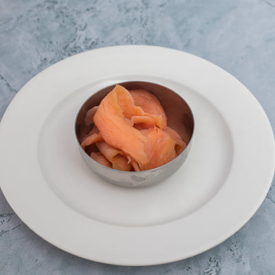 The "Keto Breakfast" from Loafology Bakery & Café features a small metal bowl filled with slices of raw salmon, elegantly presented on a white plate against a grayish background, creating a visually appealing and keto-friendly option for your low-carb diet.