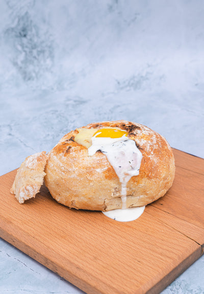 A sourdough loaf from Loafology Bakery & Café, filled with melted cheese and topped with a fried egg, served alongside shredded beef drizzled with BBQ sauce, available at Saturday and Sunday, presented on a wooden board.