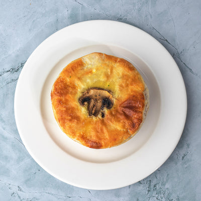 A golden-brown Vegetarian Mushroom Pie from Loafology Bakery & Café, placed on a white plate, against a light marble background.