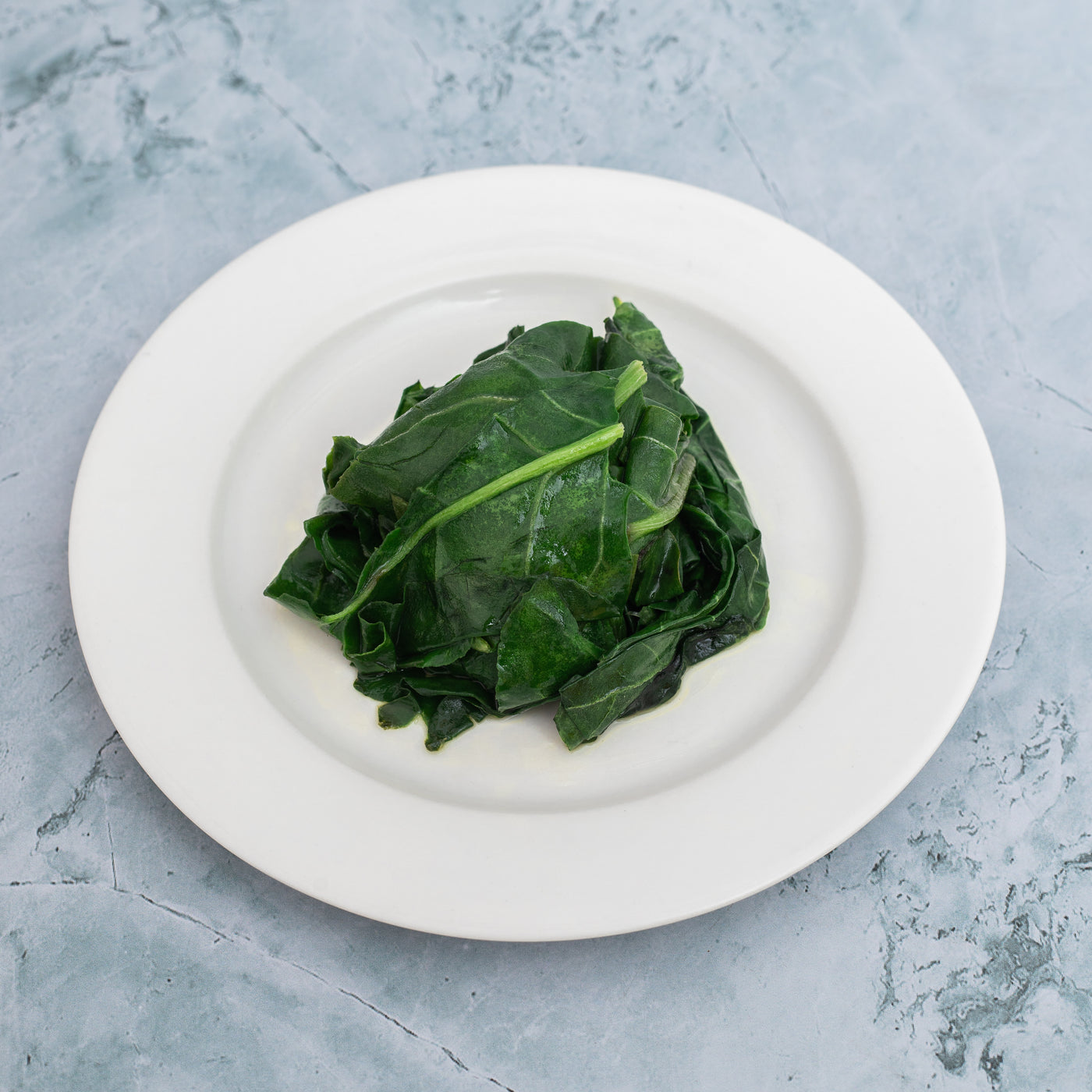 A plate with a serving of Wilted Spinach from Loafology Bakery & Café on a blue-gray textured background.