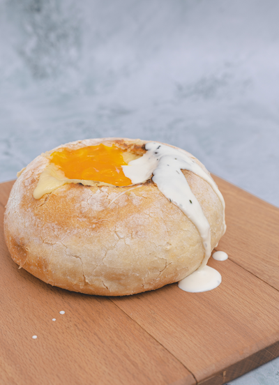 A loaf of Loafology Bakery & Café's "Vegetarian" available on Saturdays and Sundays, filled with melted cheese and a creamy white sauce, is displayed on a wooden surface.